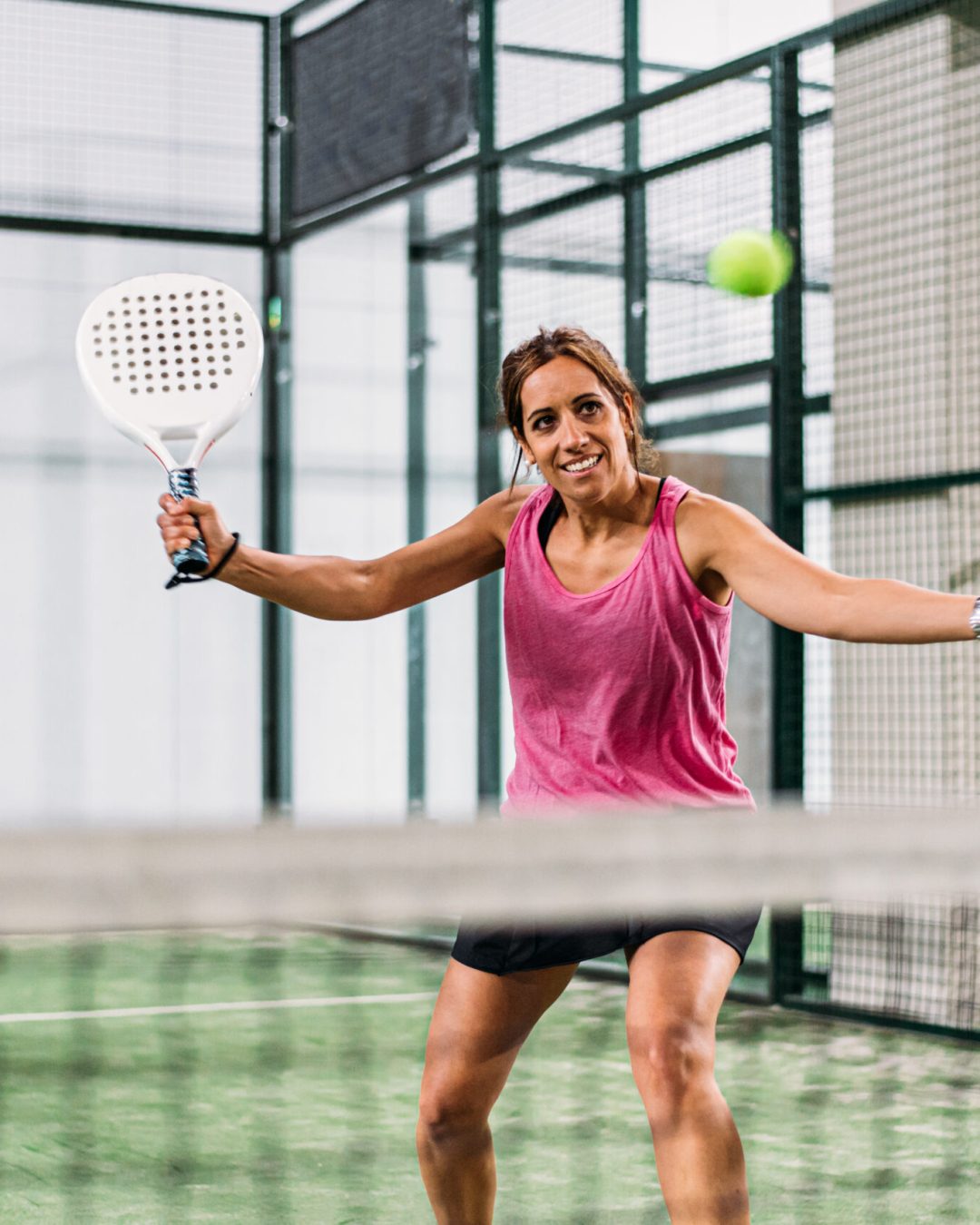 Woman playing padel in a green grass padel court indoor behind the net